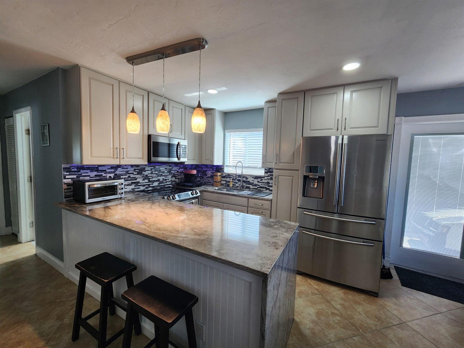 A kitchen features light gray cabinets, granite countertops, stainless steel appliances, and a tiled backsplash — 2016 Kenwood Road, West Palm Beach FL 33409, WEST PALM BEACH, FL