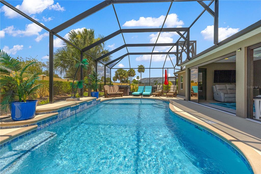 A screened-in swimming pool with a tiled spillover spa sits on a concrete patio — 1116 MAYNARD PATH, THE VILLAGES, FL