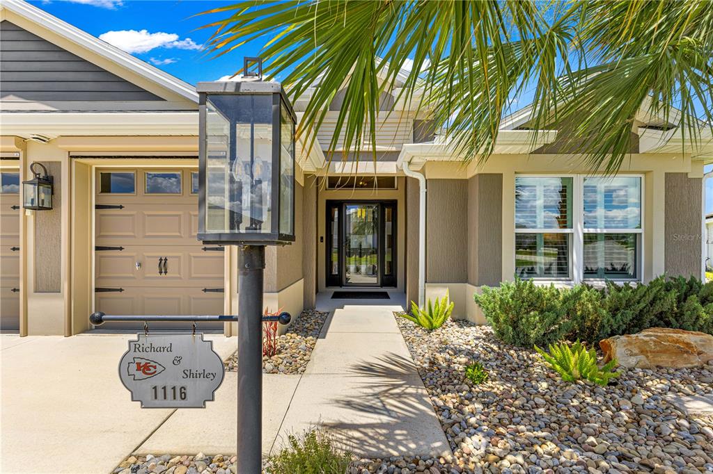 The exterior of a house features a tan facade, a garage, and a personalized sign — 1116 MAYNARD PATH, THE VILLAGES, FL
