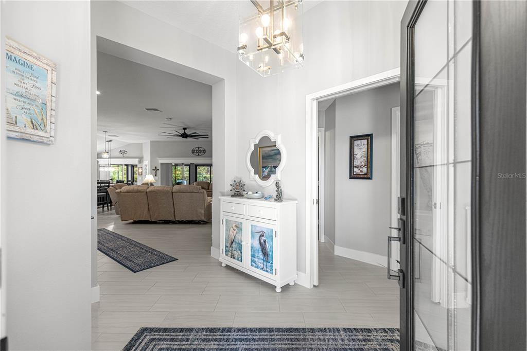 An entryway with light tile floors, a white console table, and a modern glass chandelier — 1116 MAYNARD PATH, THE VILLAGES, FL