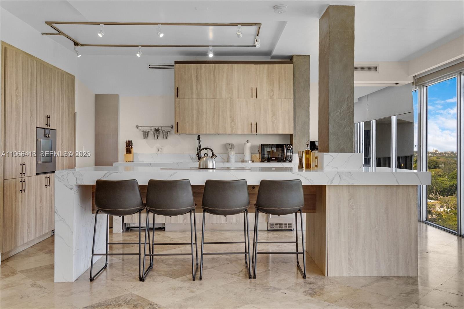 A modern kitchen features light wood cabinets, a marble-topped island with four stools, and tile flooring — 5781 Biscayne Blvd # 3, Miami FL 33137, MIAMI, FL