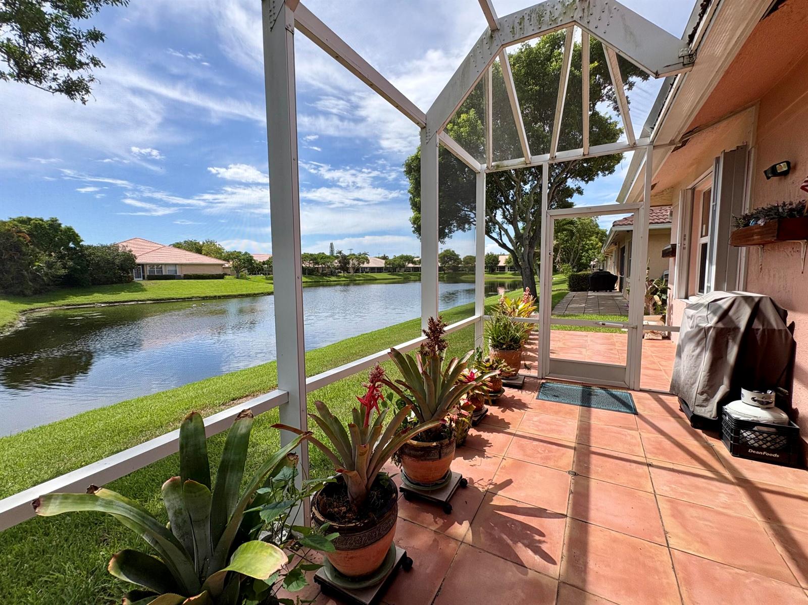 A screened-in patio with tile flooring overlooks a lake and neighboring houses — 315 Coral Trace Lane, Delray Beach FL 33445, DELRAY BEACH, FL