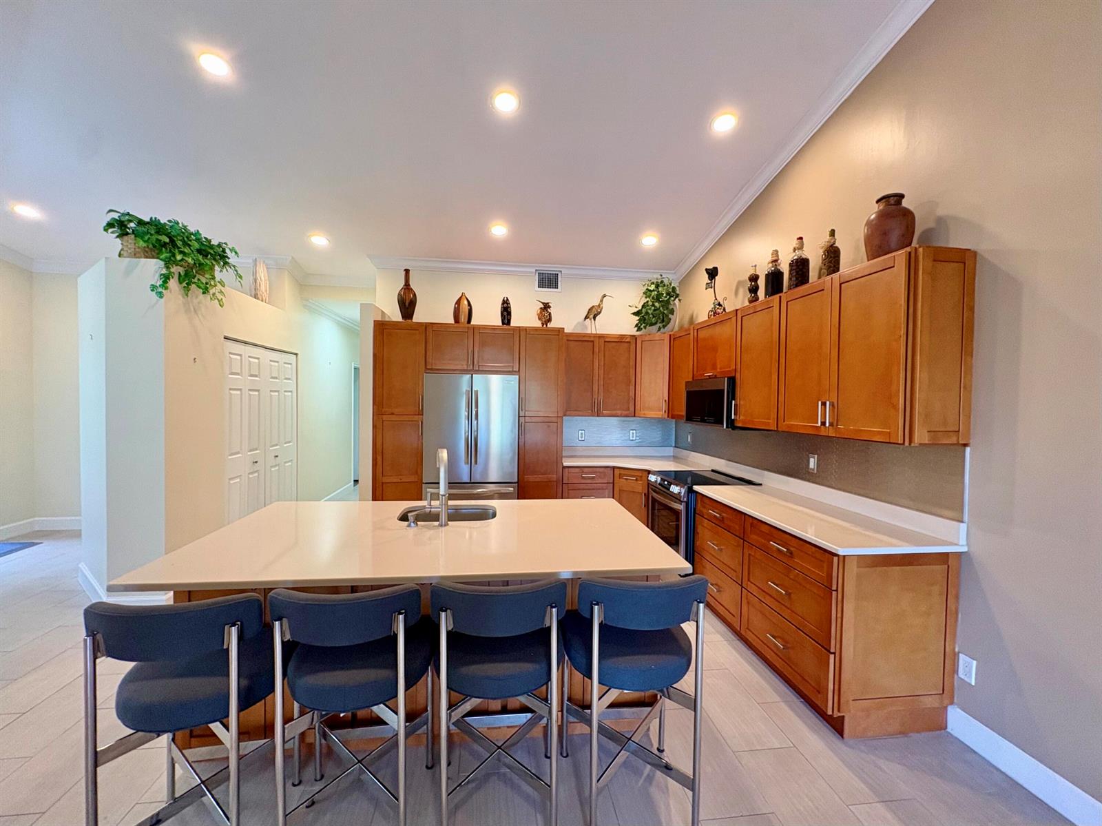 A kitchen features wood cabinets, a large island with four stools, and stainless steel appliances — 315 Coral Trace Lane, Delray Beach FL 33445, DELRAY BEACH, FL