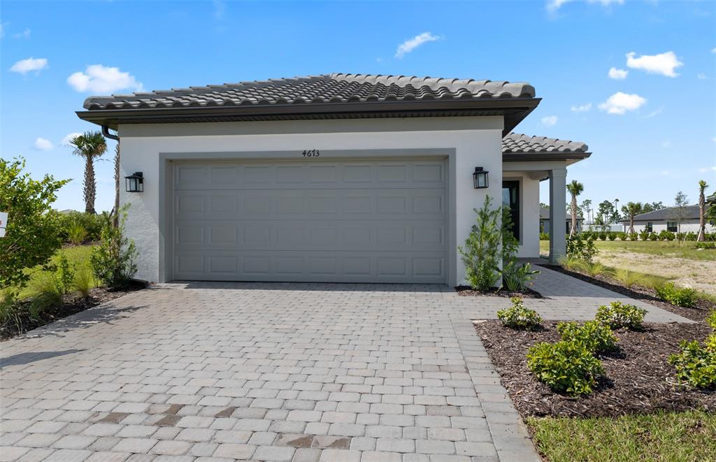 A light-colored house with a paved driveway and a two-car garage under a blue sky — 4695 BLUE STAR COURT, NORTH PORT, FL