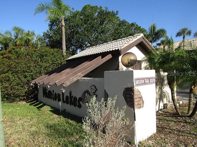 A stucco entrance sign for Mission Lakes features a wooden pergola and a spherical light — 255 MISSION TRAIL S UNIT E, VENICE, FL
