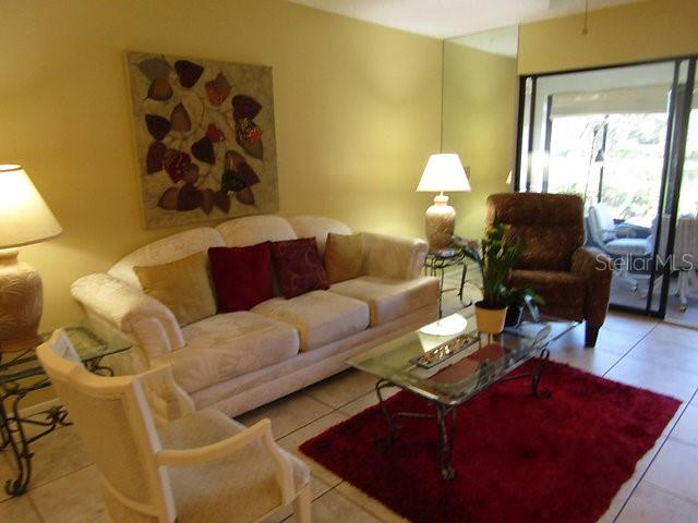 A living room features a beige sofa, a glass coffee table, and a red rug — 255 MISSION TRAIL S UNIT E, VENICE, FL