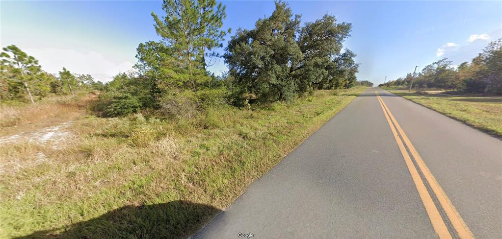 A paved road runs alongside a grassy, wooded lot under a clear blue sky — 1107 LAKEVIEW TRAIL, INTERLACHEN, FL