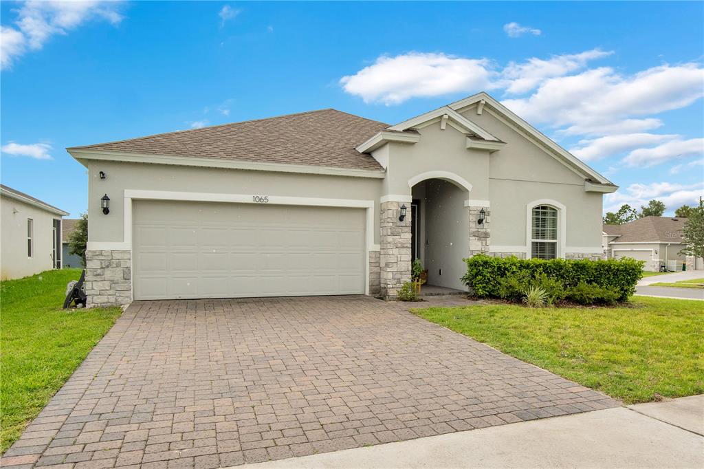 A single-story house with a beige stucco exterior, stone accents, and a paved driveway — 1065 CHELAN FALLS DRIVE, DELAND, FL