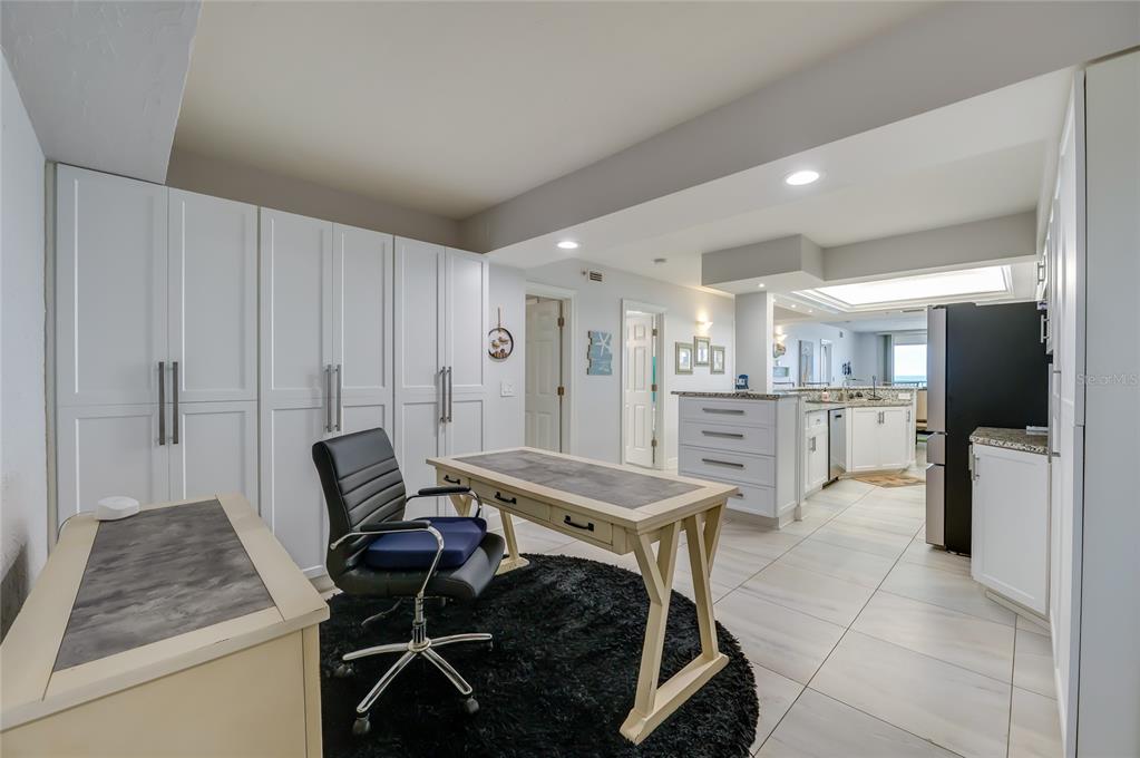 A home office with white cabinetry and a desk sits adjacent to an open kitchen — 4575 S ATLANTIC AVENUE UNIT 6304, PONCE INLET, FL