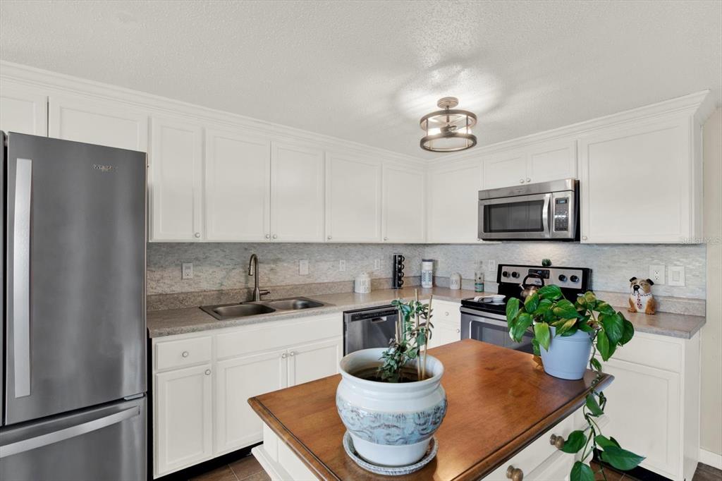 A kitchen features white cabinets, stainless steel appliances, a gray countertop, and a wooden island — 5642 DOVE DRIVE, NEW PORT RICHEY, FL
