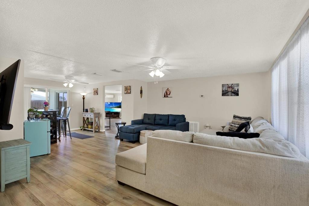A living room features a large sectional sofa, wood-look flooring, and an open dining area — 5642 DOVE DRIVE, NEW PORT RICHEY, FL