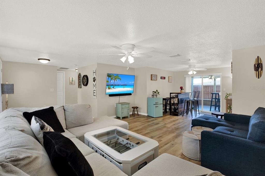 A spacious living room features light-colored walls, wood-look flooring, two ceiling fans, and sliding doors — 5642 DOVE DRIVE, NEW PORT RICHEY, FL