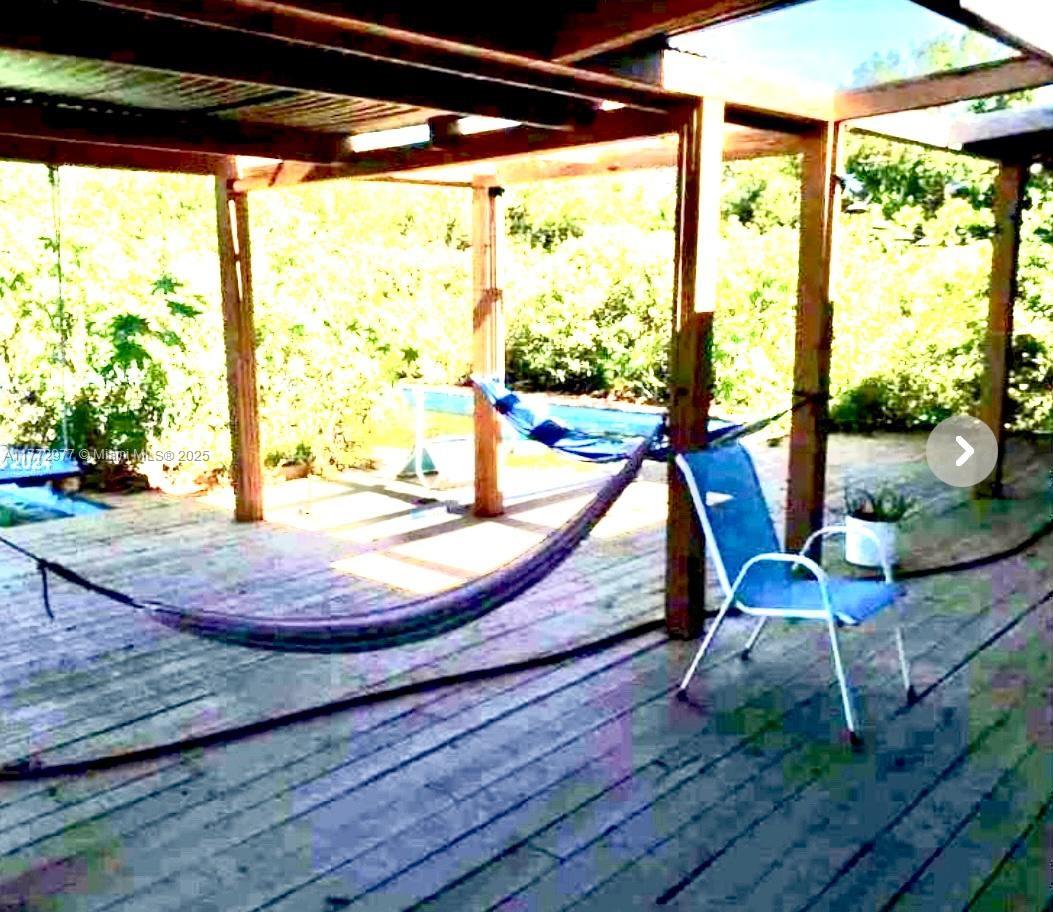 A wooden deck features a hammock and a blue chair under a covered patio structure — 312 St, Homestead FL 33033, HOMESTEAD, FL