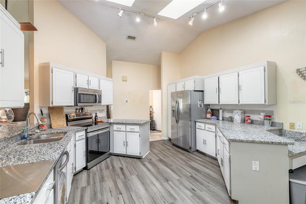 A kitchen featuring white cabinets, granite countertops, stainless steel appliances, and wood-look flooring — 50 FLORIDA PARK DRIVE, PALM COAST, FL