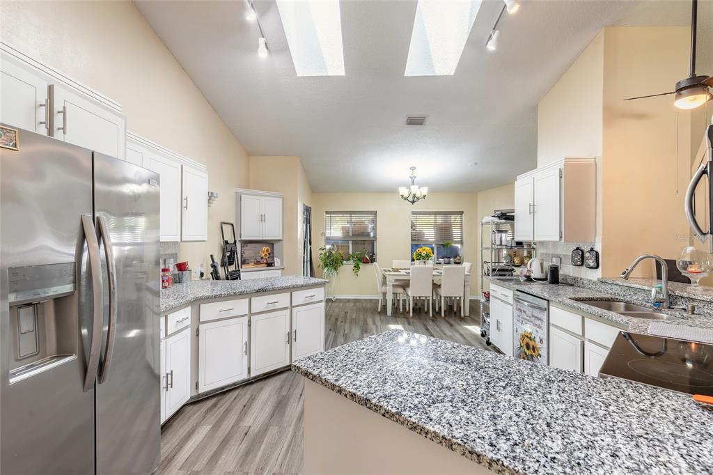 A kitchen with white cabinets, granite countertops, and stainless steel appliances opens to a dining area — 50 FLORIDA PARK DRIVE, PALM COAST, FL