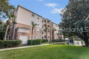 A multi-story apartment building with tan stucco siding stands next to a small pond — 1357 VENEZIA COURT UNIT 302, DAVENPORT, FL