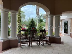Three wooden rocking chairs sit on a covered patio with white columns and tiled flooring — 1357 VENEZIA COURT UNIT 302, DAVENPORT, FL