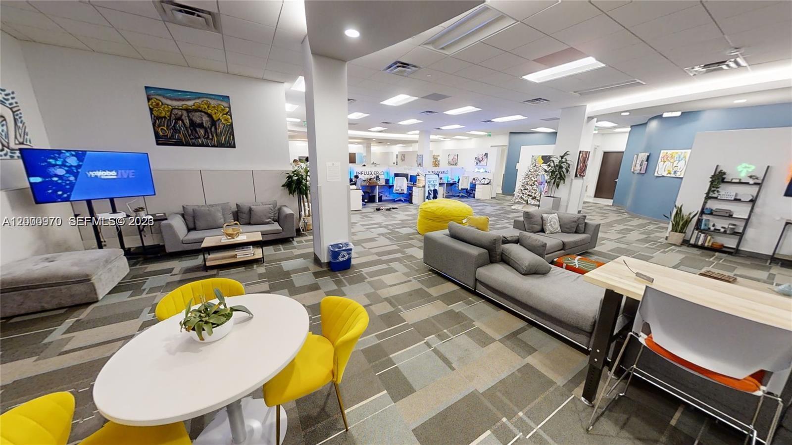 A modern office lounge area features gray sofas, yellow chairs, and a small dining table — 1501 Biscayne Blvd # 501D, Miami FL 33132, MIAMI, FL