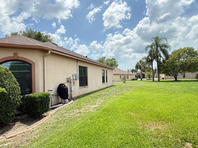 The side exterior of a beige stucco house features a large lawn and palm trees — 13743 BRYNDLEWOOD COURT, HUDSON, FL