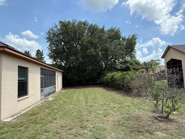 A grassy backyard sits between two beige houses with a large tree in the background — 13743 BRYNDLEWOOD COURT, HUDSON, FL