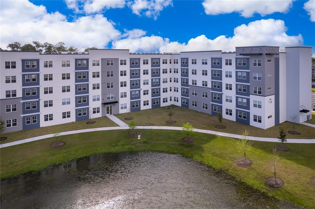 An aerial view of a multi-story apartment building with a central courtyard and pond — 5587 MILLENIA PARK BLVD UNIT 113, ORLANDO, FL