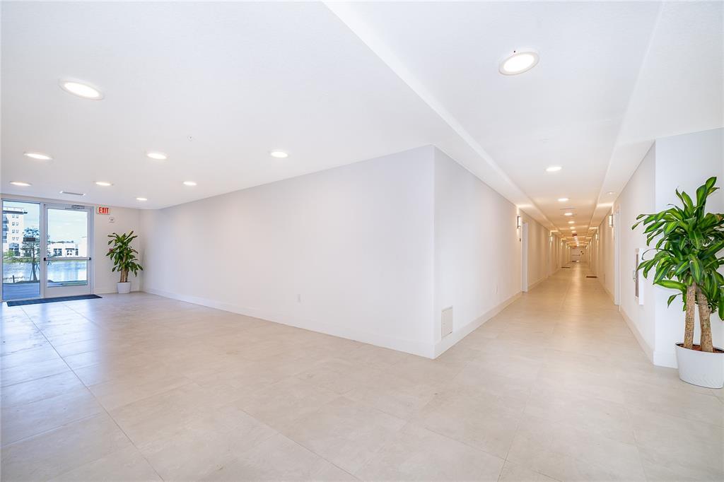 A bright, tiled hallway features recessed lighting, white walls, and two potted green plants — 5587 MILLENIA PARK BLVD UNIT 113, ORLANDO, FL