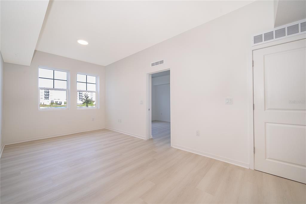 An empty room features light wood-look flooring, white walls, two windows, and a doorway — 5587 MILLENIA PARK BLVD UNIT 113, ORLANDO, FL