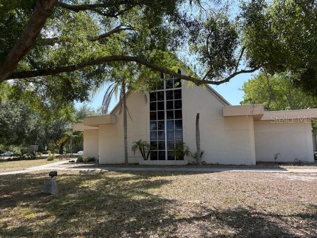 A white A-frame building with a large glass window facade stands under mature trees — 112 N LOCKMOOR AVENUE, TEMPLE TERRACE, FL