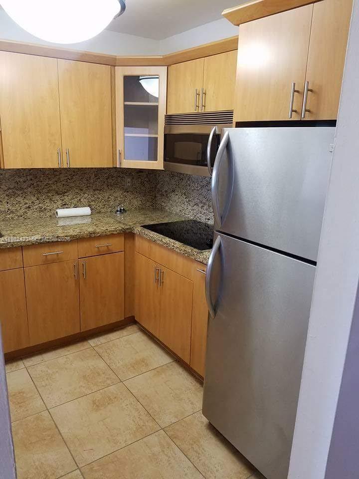 A kitchen with light wood cabinets, granite countertops, stainless steel appliances, and tiled flooring — 9682 Fontainebleau Blvd # 202, Miami FL 33172, MIAMI, FL