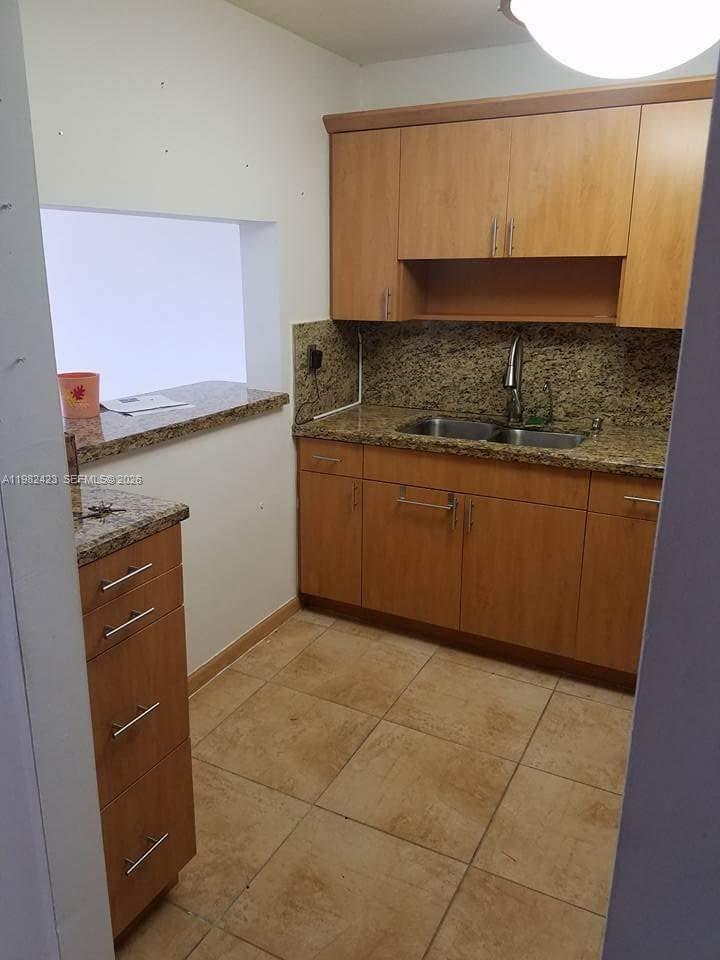 A small kitchen features light wood cabinets, granite countertops, and beige tile flooring — 9682 Fontainebleau Blvd # 202, Miami FL 33172, MIAMI, FL