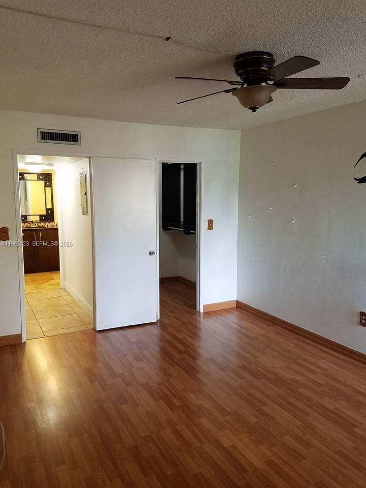 A bedroom with wood-look flooring, a ceiling fan, and doorways leading to a bathroom and closet — 9682 Fontainebleau Blvd # 202, Miami FL 33172, MIAMI, FL