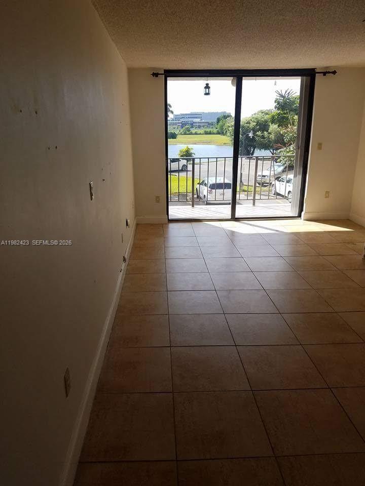 An empty room with beige tile flooring and a sliding glass door leading to a balcony — 9682 Fontainebleau Blvd # 202, Miami FL 33172, MIAMI, FL