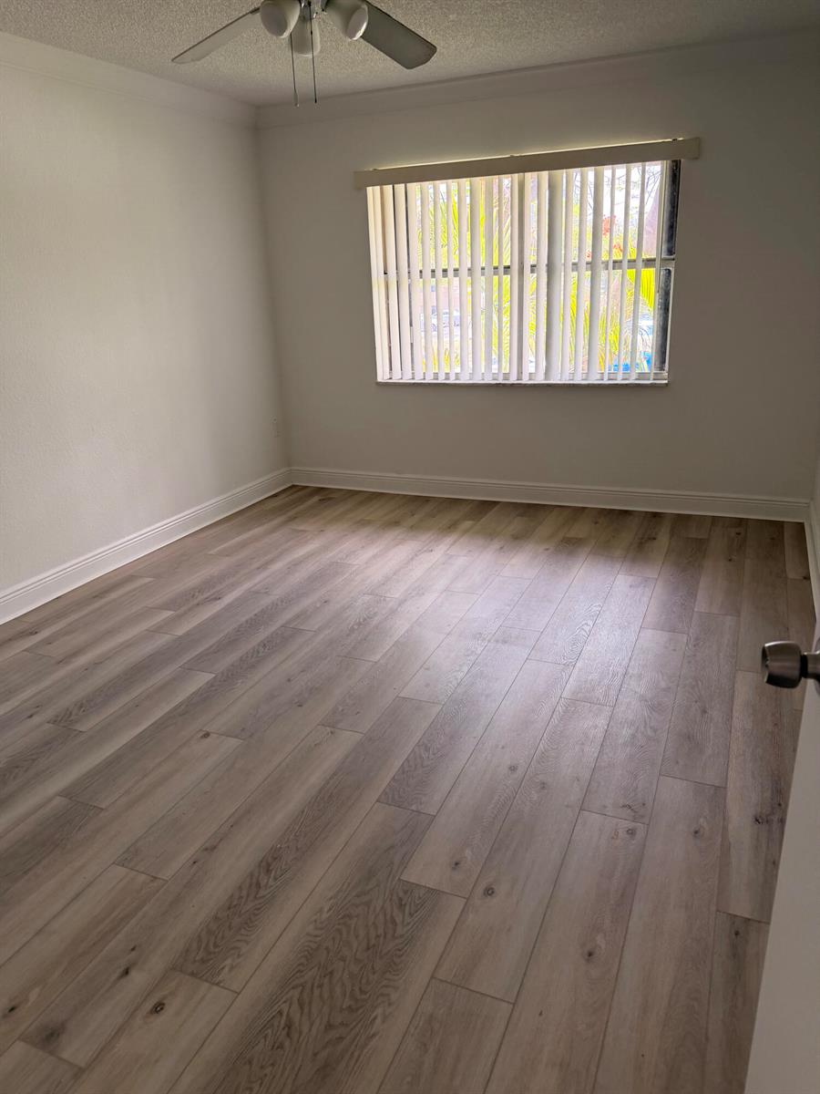 An empty bedroom features light wood-look flooring, white walls, and vertical window blinds — 10401 SW 108th Avenue # 240, Miami FL 33176, MIAMI, FL