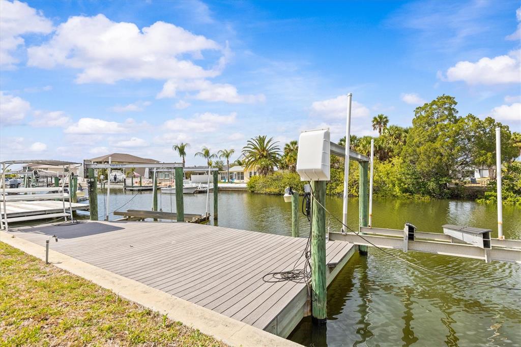 A wooden boat dock with a lift extends into a canal surrounded by lush vegetation — 7427 SOUTHWIND DRIVE, HUDSON, FL