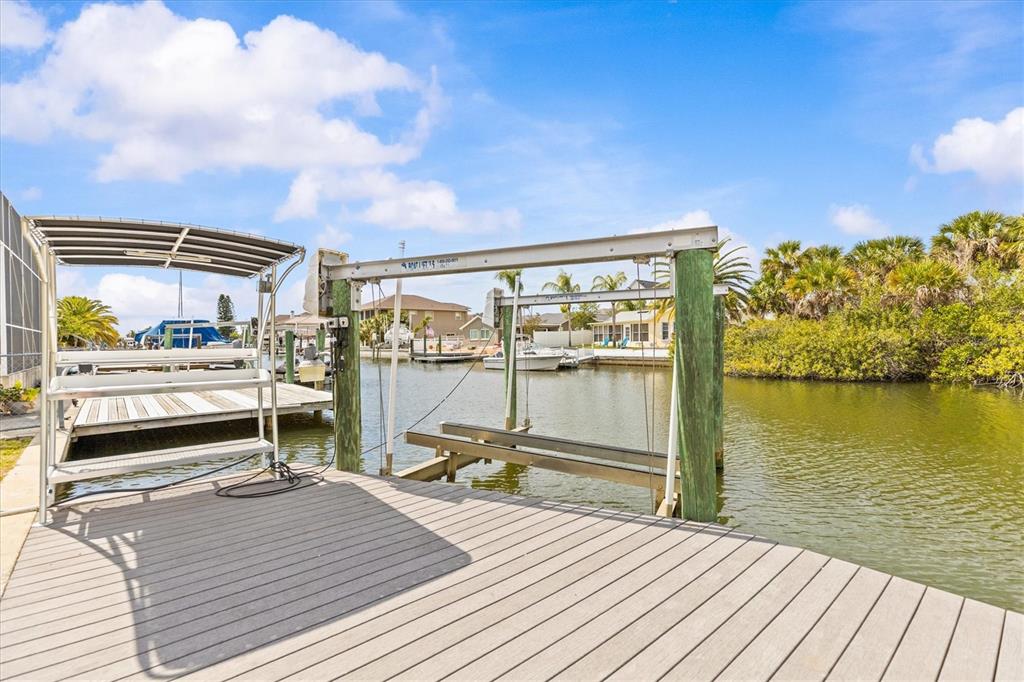 A wooden boat dock features a metal boat lift extending over a canal — 7427 SOUTHWIND DRIVE, HUDSON, FL