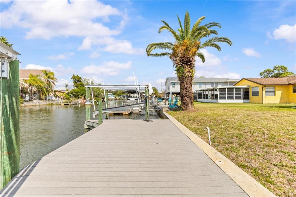 A wooden dock extends into a canal next to a palm tree and a yellow house — 7427 SOUTHWIND DRIVE, HUDSON, FL