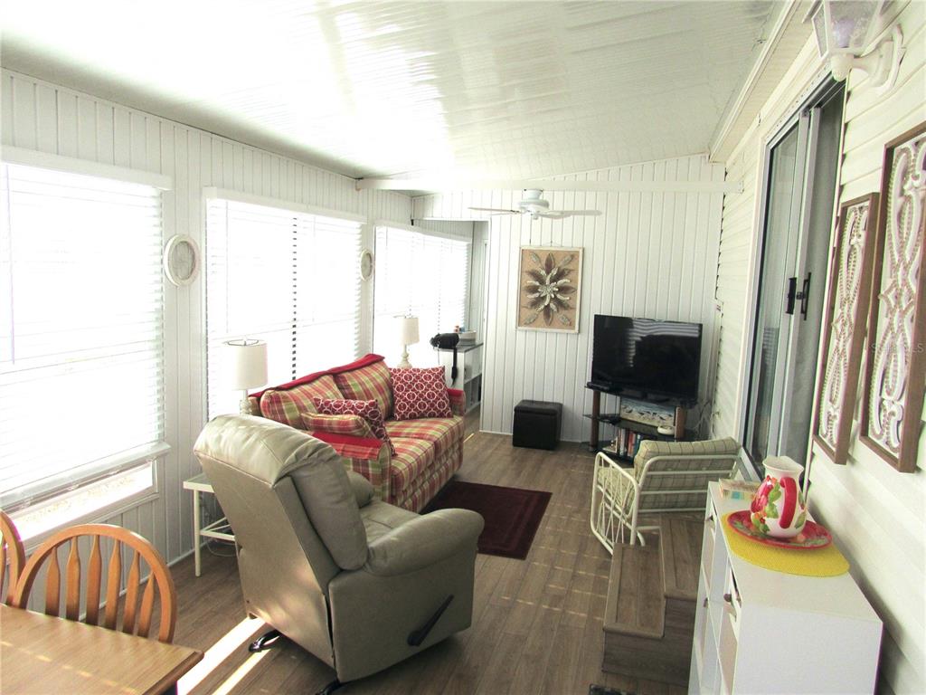 A sunroom features wood-look flooring, white paneled walls, a ceiling fan, and casual furniture — 9000 US HWY 192 UNIT 598, CLERMONT, FL
