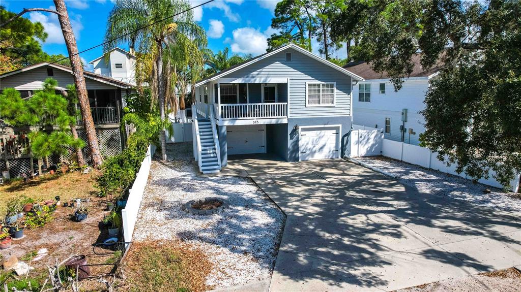 An elevated two-story house features a white garage, a front staircase, and a gravel yard — 815 FLORIDA AVENUE, PALM HARBOR, FL