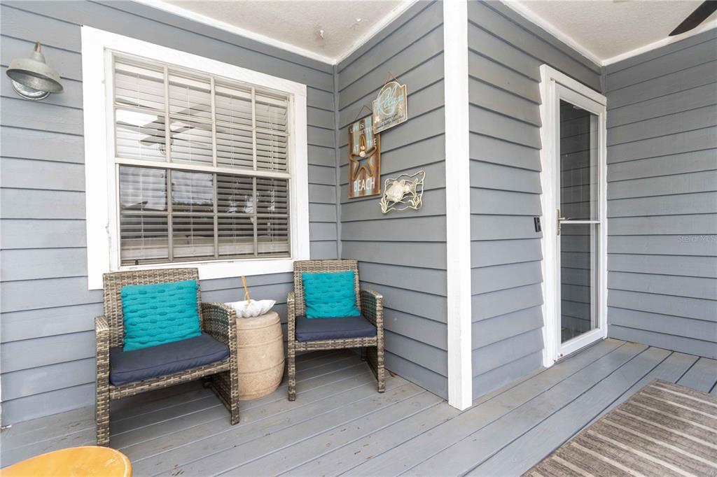 A covered porch features gray siding, two wicker chairs with teal pillows, and a window — 815 FLORIDA AVENUE, PALM HARBOR, FL