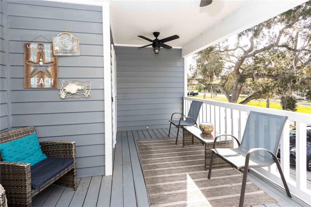 A covered outdoor balcony features gray wood siding, a ceiling fan, and patio furniture — 815 FLORIDA AVENUE, PALM HARBOR, FL