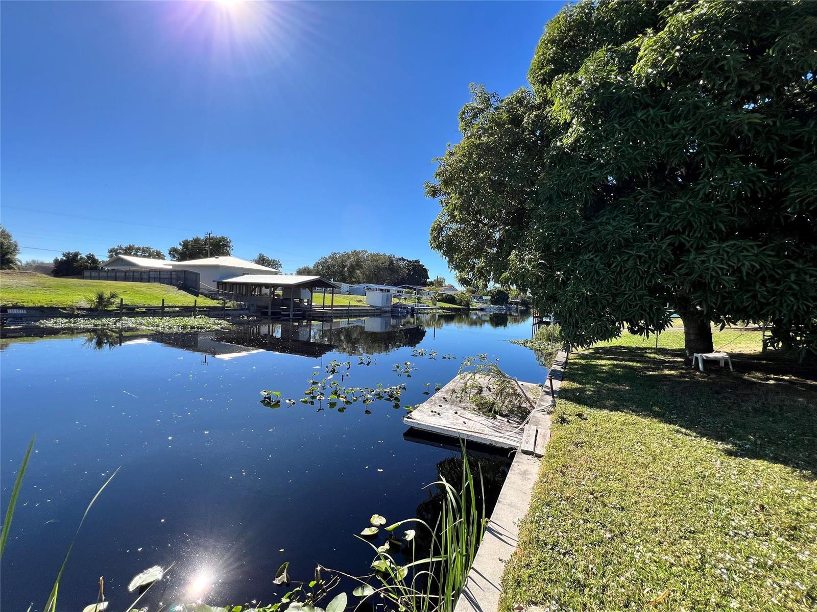 A canal view features a grassy bank, a small dock, and a large tree — 3438 SE 27th Street, Okeechobee FL 34974, OKEECHOBEE, FL