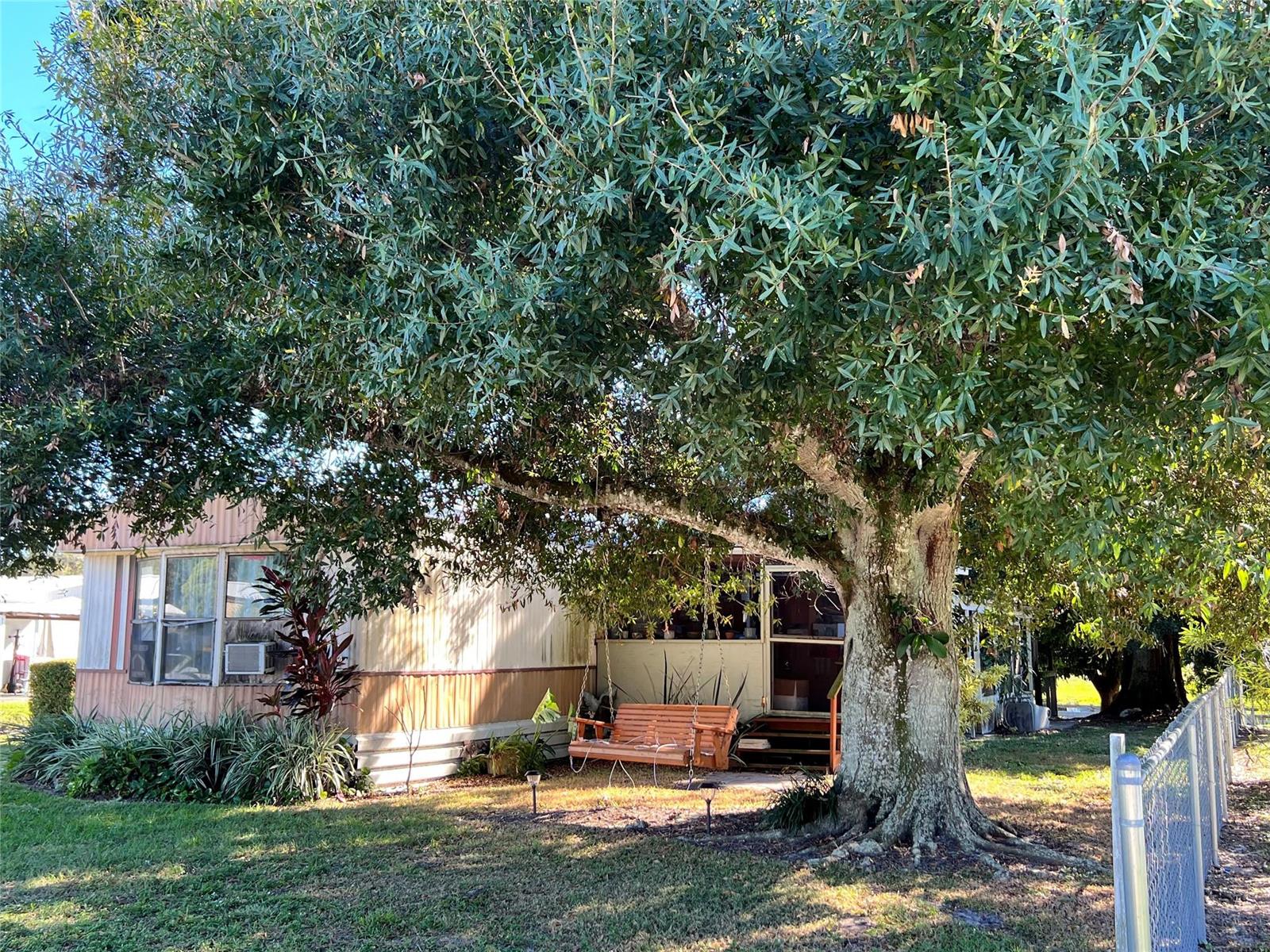 A wooden porch swing hangs under a large tree in front of a mobile home — 3438 SE 27th Street, Okeechobee FL 34974, OKEECHOBEE, FL