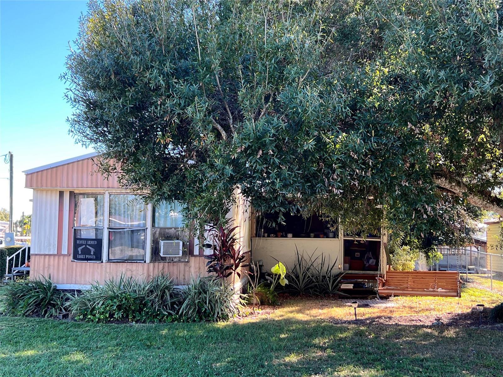 A single-story mobile home with a large tree, a front porch swing, and a yard — 3438 SE 27th Street, Okeechobee FL 34974, OKEECHOBEE, FL