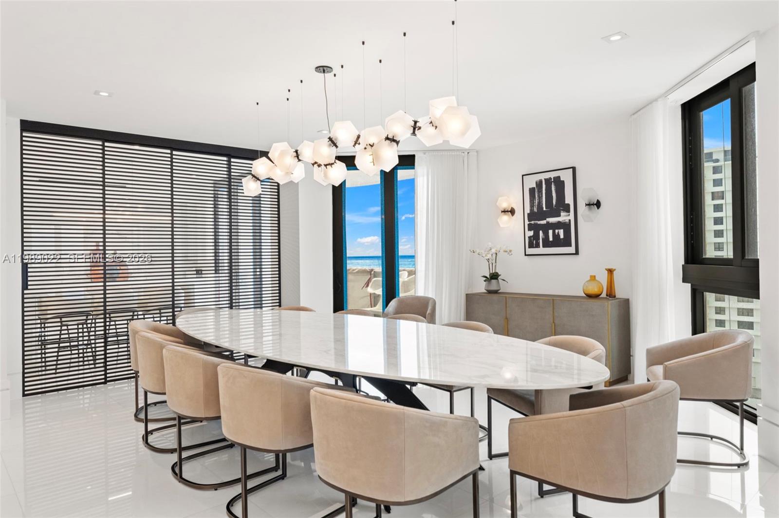 A dining room features an oval marble table, upholstered chairs, and a modern geometric chandelier — 9999 Collins Ave # 11J, Bal Harbour FL 33154, BAL HARBOUR, FL