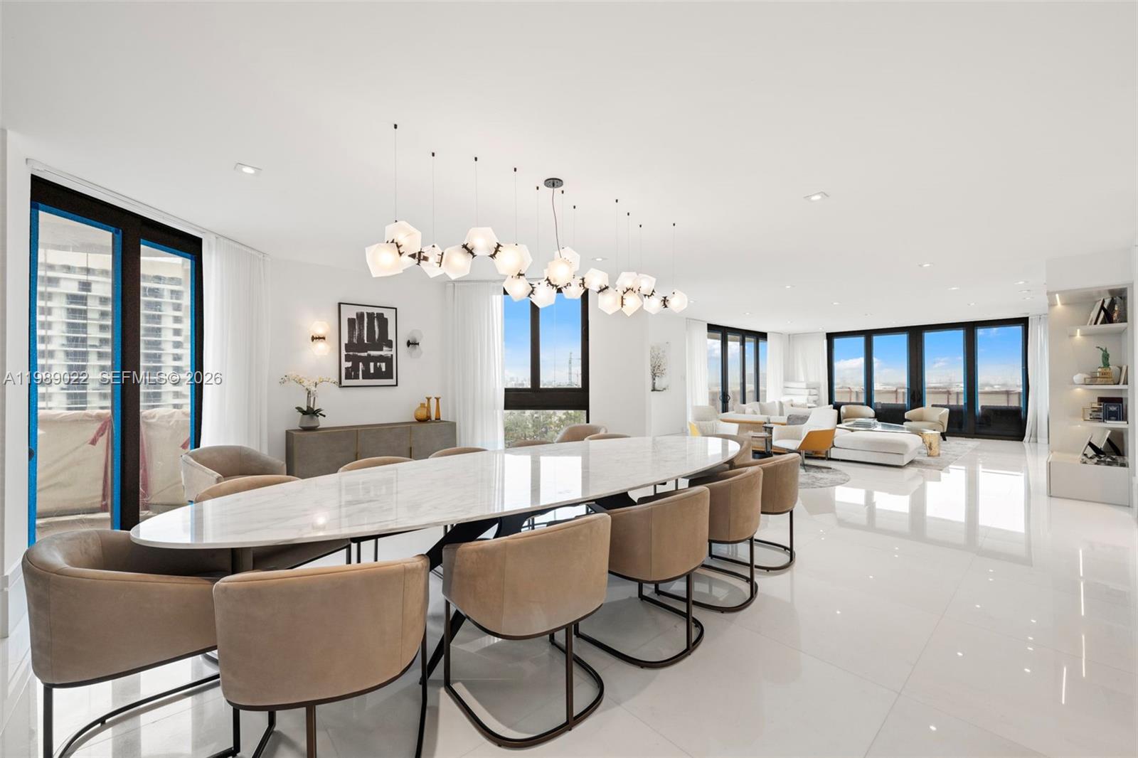 A modern dining room features a long marble table, tan chairs, and a sculptural chandelier — 9999 Collins Ave # 11J, Bal Harbour FL 33154, BAL HARBOUR, FL