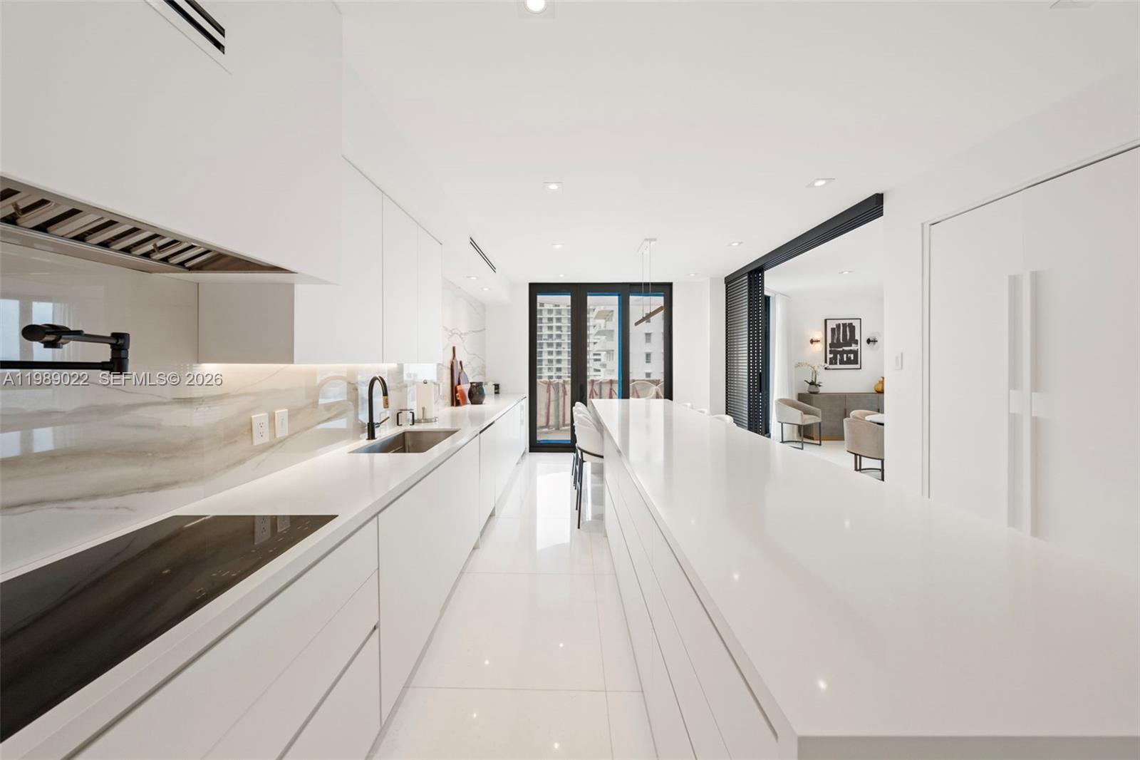 A modern white kitchen features a long island, marble backsplash, and minimalist cabinetry — 9999 Collins Ave # 11J, Bal Harbour FL 33154, BAL HARBOUR, FL
