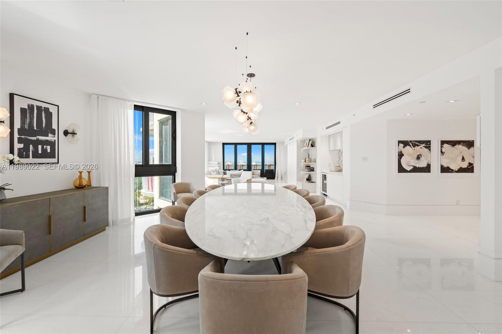 A dining room features a marble oval table, beige chairs, and a modern light fixture — 9999 Collins Ave # 11J, Bal Harbour FL 33154, BAL HARBOUR, FL