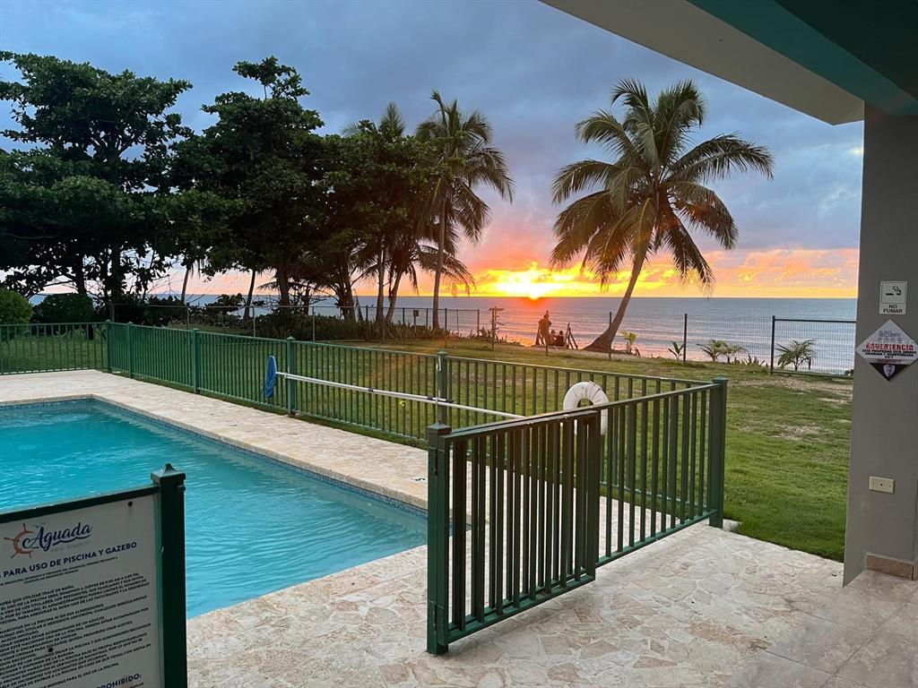 A swimming pool with a green fence overlooks the ocean at sunset with palm trees — KM 2.6 CARR 441 VILLA 14, AGUADA, PR