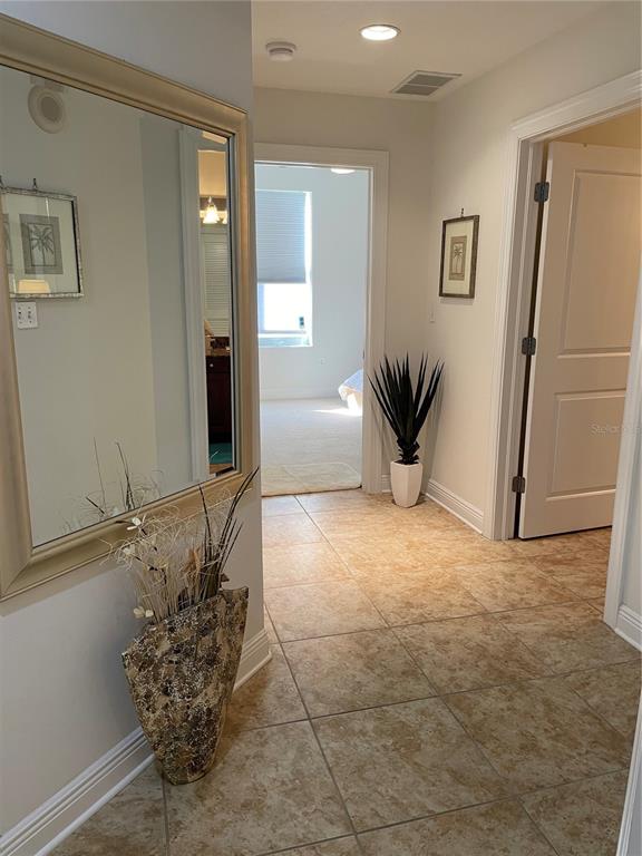 A hallway with tile flooring leads to a bedroom doorway, featuring a large wall mirror — 628 CLEVELAND STREET UNIT 1002, CLEARWATER, FL