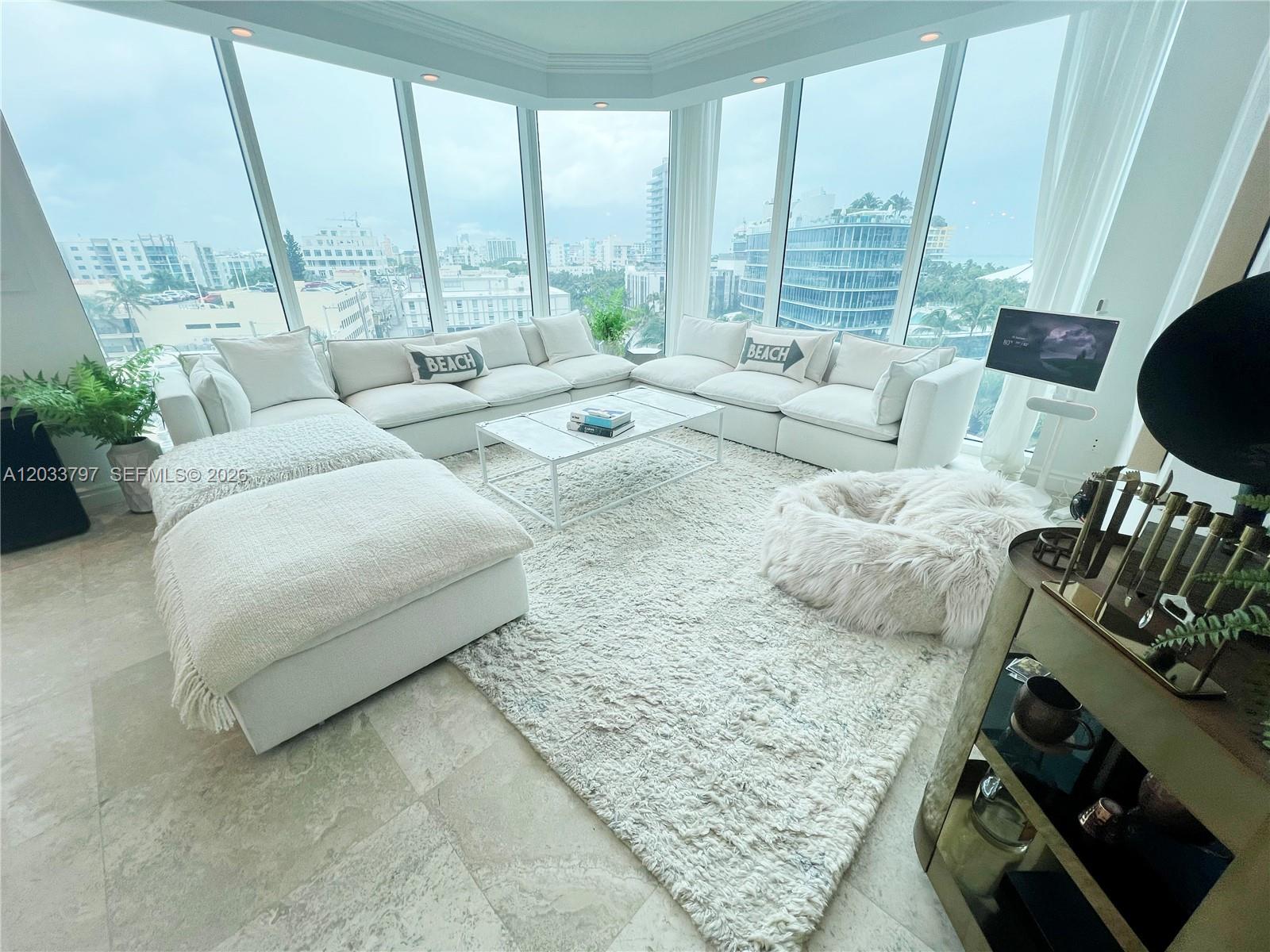A bright living room features a large white sectional, a shag rug, and floor-to-ceiling windows — 300 S Pointe Dr # 705, Miami Beach FL 33139, MIAMI BEACH, FL